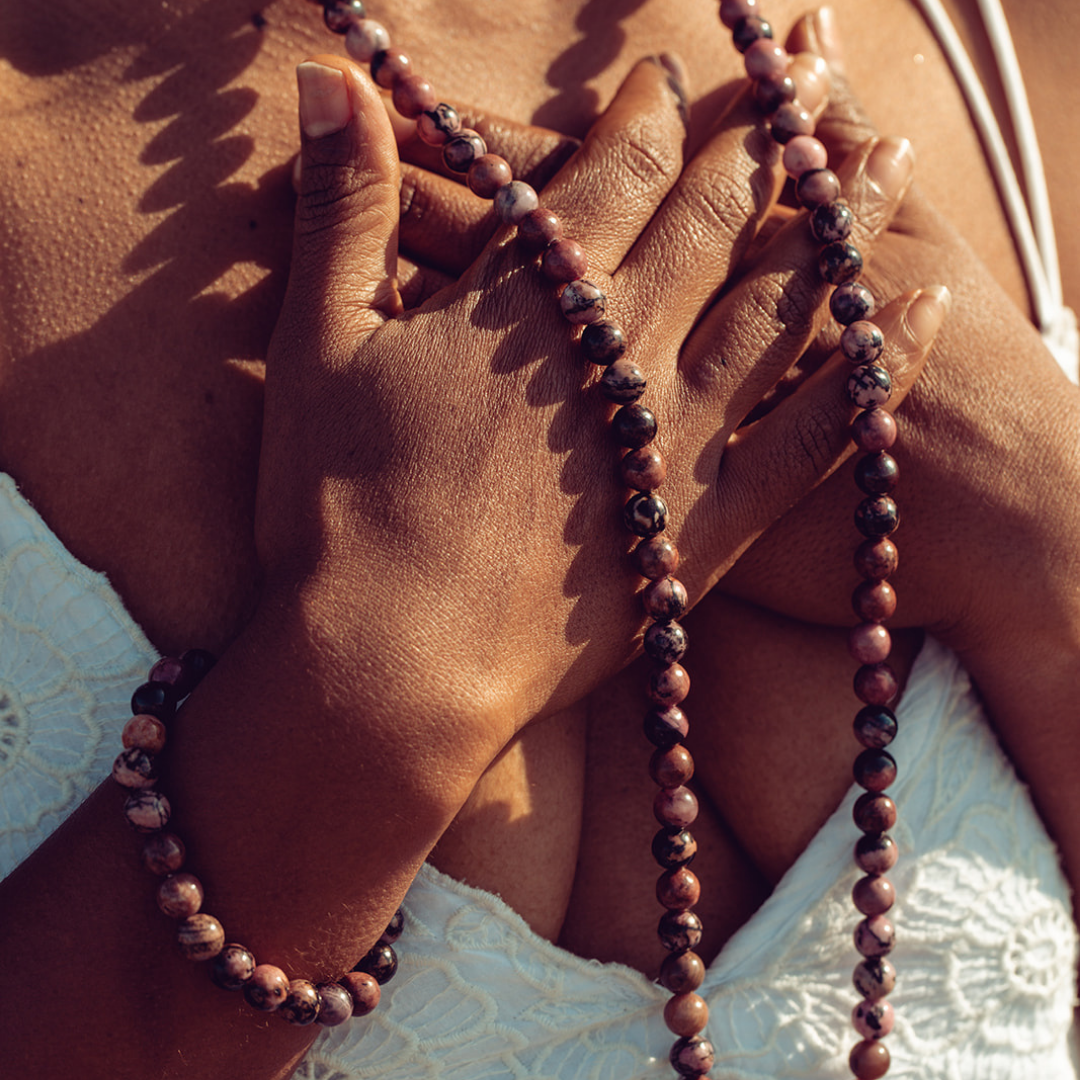 Close up of woman with hands on her chest wearing Ambarya Emotional Healing - Rhondonite Mala Bead Set