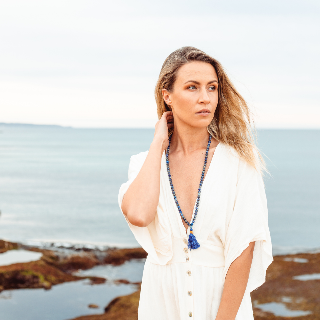 Woman with fair skin, blonde hair and a white dress, looking into the distance wearing Ambarya Wisdom - Lapis Lazuli Mala Bead Necklace